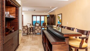 Un vaste espace dédié à la salle à manger, avec une longue table et des chaises, un buffet en bois contenant de la verrerie, et une vue sur la mer grâce à de grandes fenêtres.