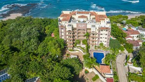 Un hôtel à plusieurs étages doté d’une piscine, entouré d’une végétation luxuriante et situé près d’une plage.
