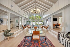 A spacious dining area with a high ceiling, a chandelier, and a large window providing natural light.