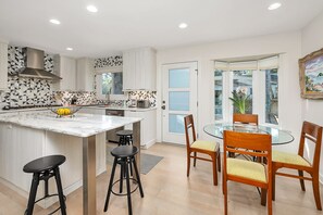 A modern kitchen with a marble island, black bar stools, and a dining area with wooden chairs and a glass table.