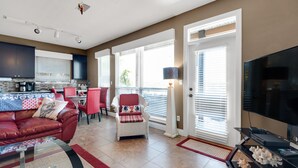 A modern living room with a red leather couch, a glass coffee table, and a dining area with red chairs. There is a kitchen with dark cabinets and a large window. - Ocean view, walk to the beach, pool,  military/first responder discount 13A (Destin)