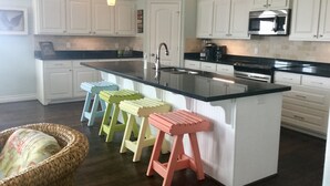 Una cocina con armarios blancos, encimera negra y una isla central con taburetes.