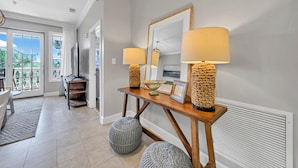 A modern living room with a wooden console table, two lamps, a mirror, and a view of the outdoors through a sliding glass door. - Overlooking 30A!  Great Location! Easy Beach & Pool Access! (Seacrest Beach)