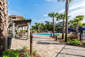 Relax by the pool surrounded by palm trees and lounge chairs, with a pergola offering additional seating and a pathway leading to the water.