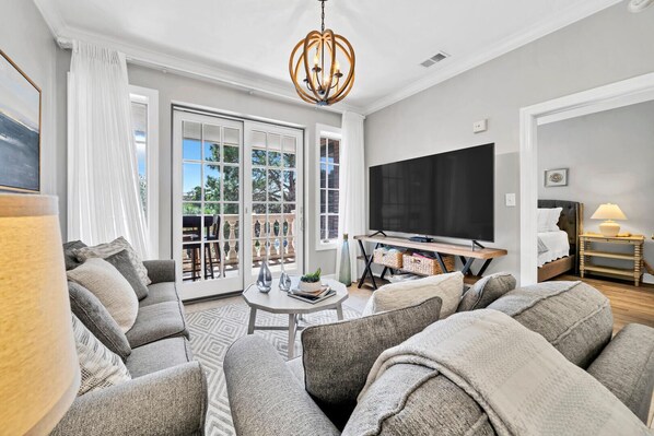 A modern living room with a sofa set, a coffee table, a TV, and a balcony with a view.