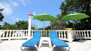 Un área de piscina con dos sillas reclinables azules y dos sombrillas verdes.