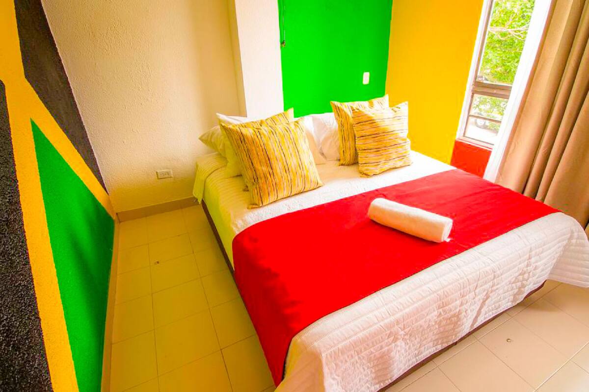 A hotel room with a bed, a green wall, a yellow wall, and a window with curtains.
