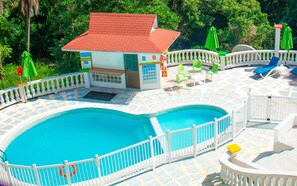 Un área de piscina con un pequeño edificio, sillas de descanso y una valla blanca.