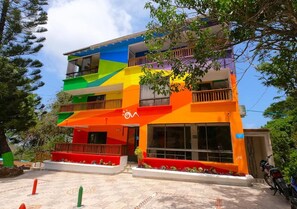 Un edificio de varios pisos con balcones y ventanas amplias, rodeado de árboles y un cielo despejado.