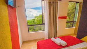 Una habitación de hotel con una cama, un ventanal con vistas a la vegetación y una pared roja y amarilla.