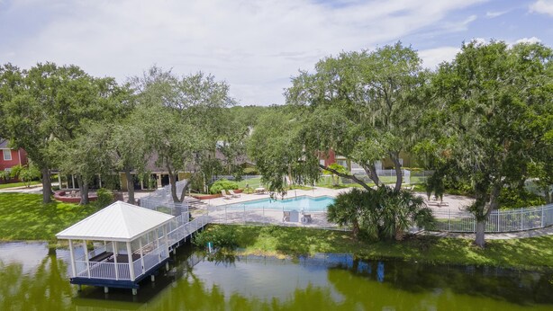 Vista de un lago con un muelle, piscina y árboles circundantes.