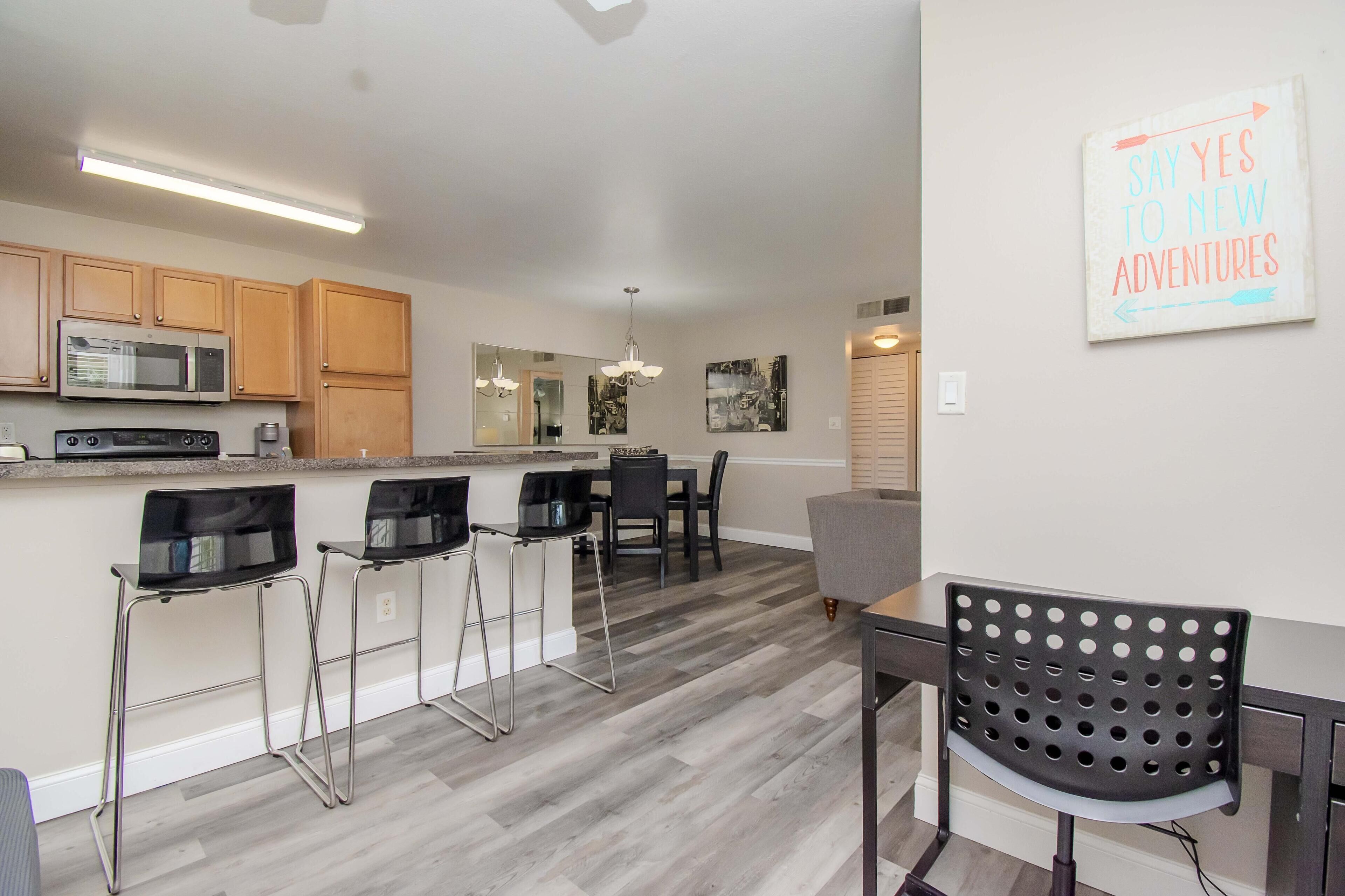 A modern kitchen with wooden cabinets, a microwave, and a dining area with bar stools and a table.