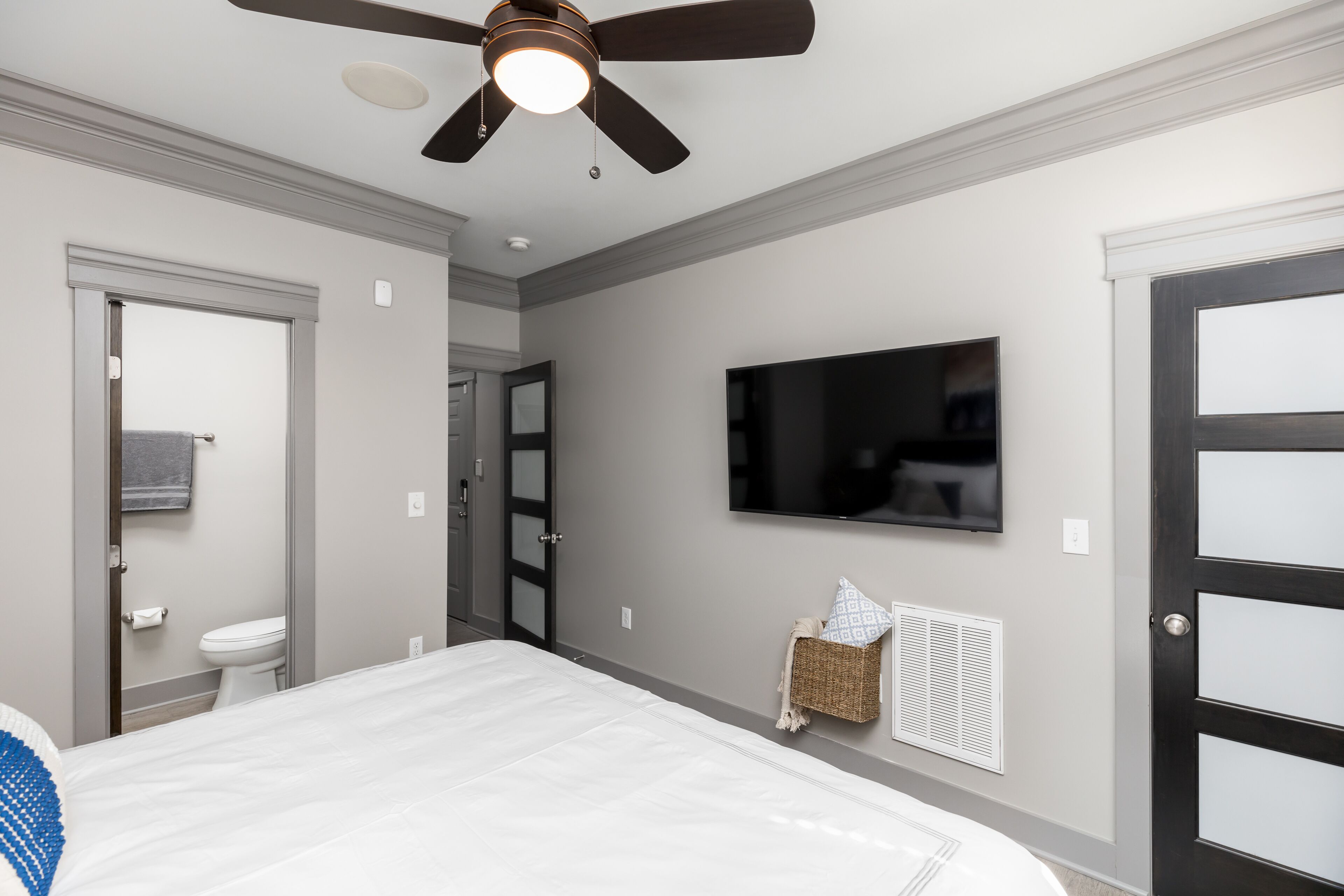 A bedroom with a bed, a ceiling fan, a television mounted on the wall, and a door with frosted glass panels.