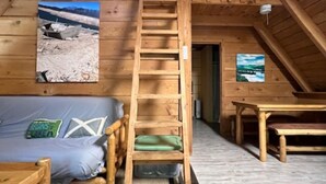Ein gemütliches Schlafzimmer im Dachgeschoss mit einer Holzleiter, die zu einem Schlafpodest führt, einem Etagenbett, einem kleinen Tisch und einem gerahmten Bild an der Wand.