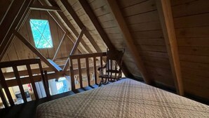 Ein Schlafzimmer mit Holzboden und geneigter Decke, einem Bett mit gemustertem Überwurf und einem Fenster mit Blick ins Freie.