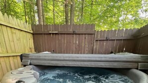 Ein Whirlpool in einer Außenanlage mit Holzlattenzaun und Bäumen im Hintergrund.