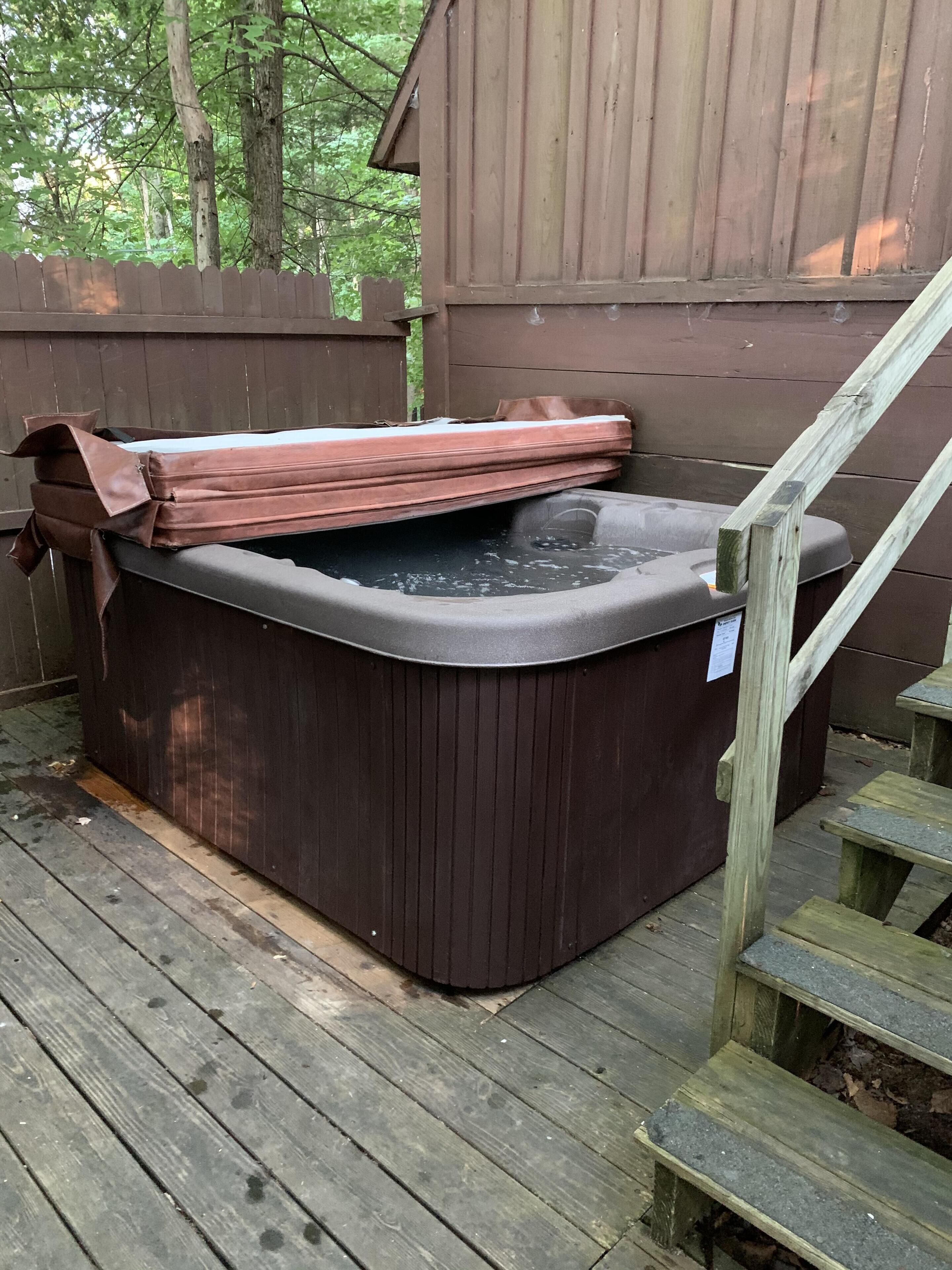 Un bain à remous sur une terrasse en bois, avec une clôture en bois et des escaliers menant à un bâtiment.
