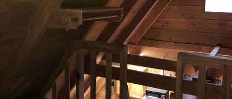 A wooden attic bedroom with a sloped ceiling, a small window, and a bed with a white mattress.