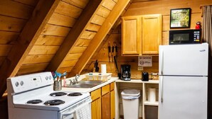 A compact kitchen with wooden cabinets, a stove, a sink, a microwave, and a refrigerator. - Reel Simple - Pet Friendly with Hot Tub (Summersville)
