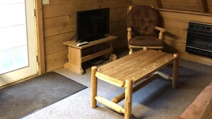A wooden interior with a television on a wooden stand, a leather armchair, and a wooden table. - Reel Simple - Pet Friendly with Hot Tub (Summersville)