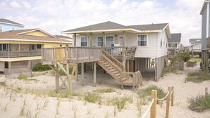 Ett hus vid stranden med en träterrass och en trappa som leder upp till huvudentrén.