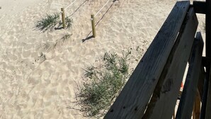 En strand med ett trästaket och en bänk, som leder ner till havet.