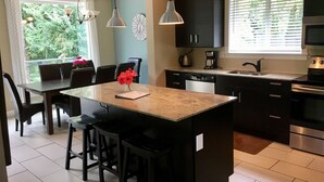 Eine moderne Küche mit Kochinsel, schwarzen Schränken, Edelstahlgeräten und einem Essbereich mit Stühlen und einem Tisch.