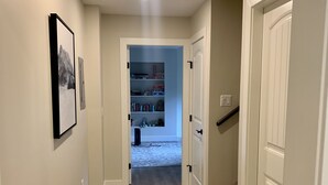 Ein Korridor mit Holzboden, weißen Wänden und einer Tür zu einem Zimmer mit Bett und Kommode.