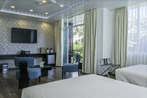 Una habitación de hotel con una cama grande, dos sillones, una mesita y un televisor montado en una pared con dise ño, además de un balcón con cortinas.