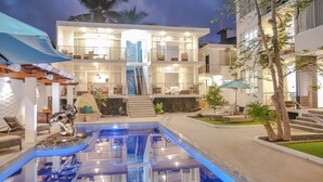 Un hotel moderno con piscina, mobiliario exterior e interiores bien iluminados.
