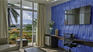 Una habitación de hotel moderna con un gran ventanal, un televisor de pantalla plana, un escritorio, una silla y una planta en maceta.