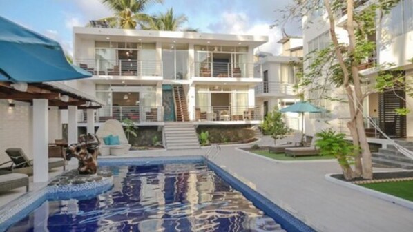 A modern multi-story building with a swimming pool, outdoor seating, and palm trees. - Ikala Galapagos Hotel (Puerto Ayora)