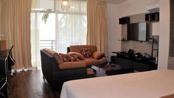 A hotel room with a bed, a sofa, a dining table, and a kitchen area.