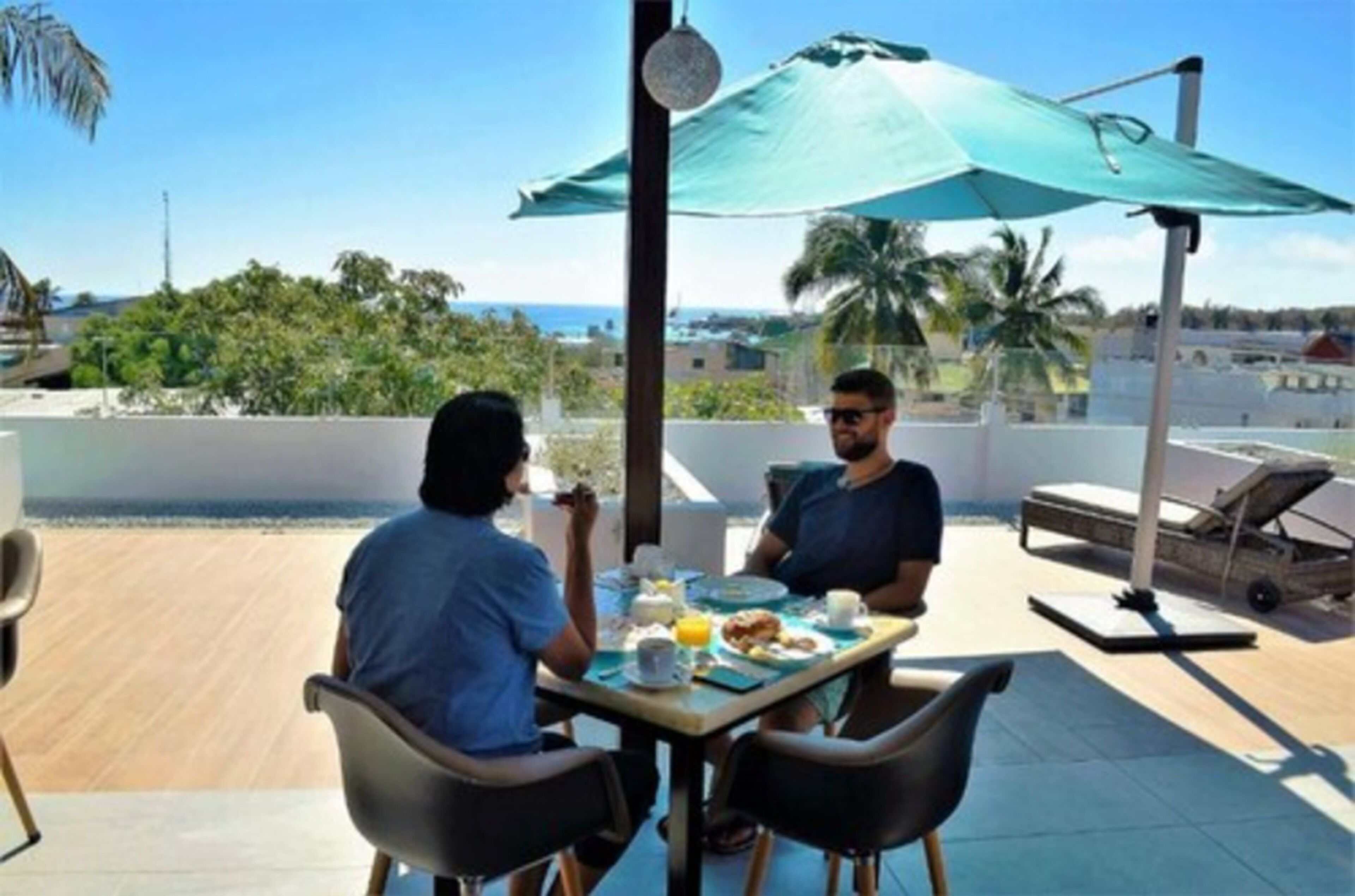 Two people dining at an outdoor table with a view of the beach and palm trees.