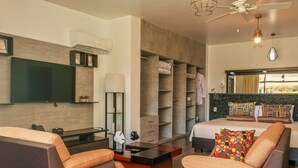 Habitación de hotel moderna con una cama grande, dos sofás, televisor, armario y vistas al balcón.