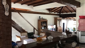 Ein geräumiger Wohnbereich mit einer Holztreppe, einem Esstisch mit Stühlen, einer Küchenzeile und Blick ins Freie.