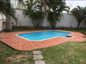 Una piscina rectangular con borde de ladrillo, rodeada de césped y palmeras.