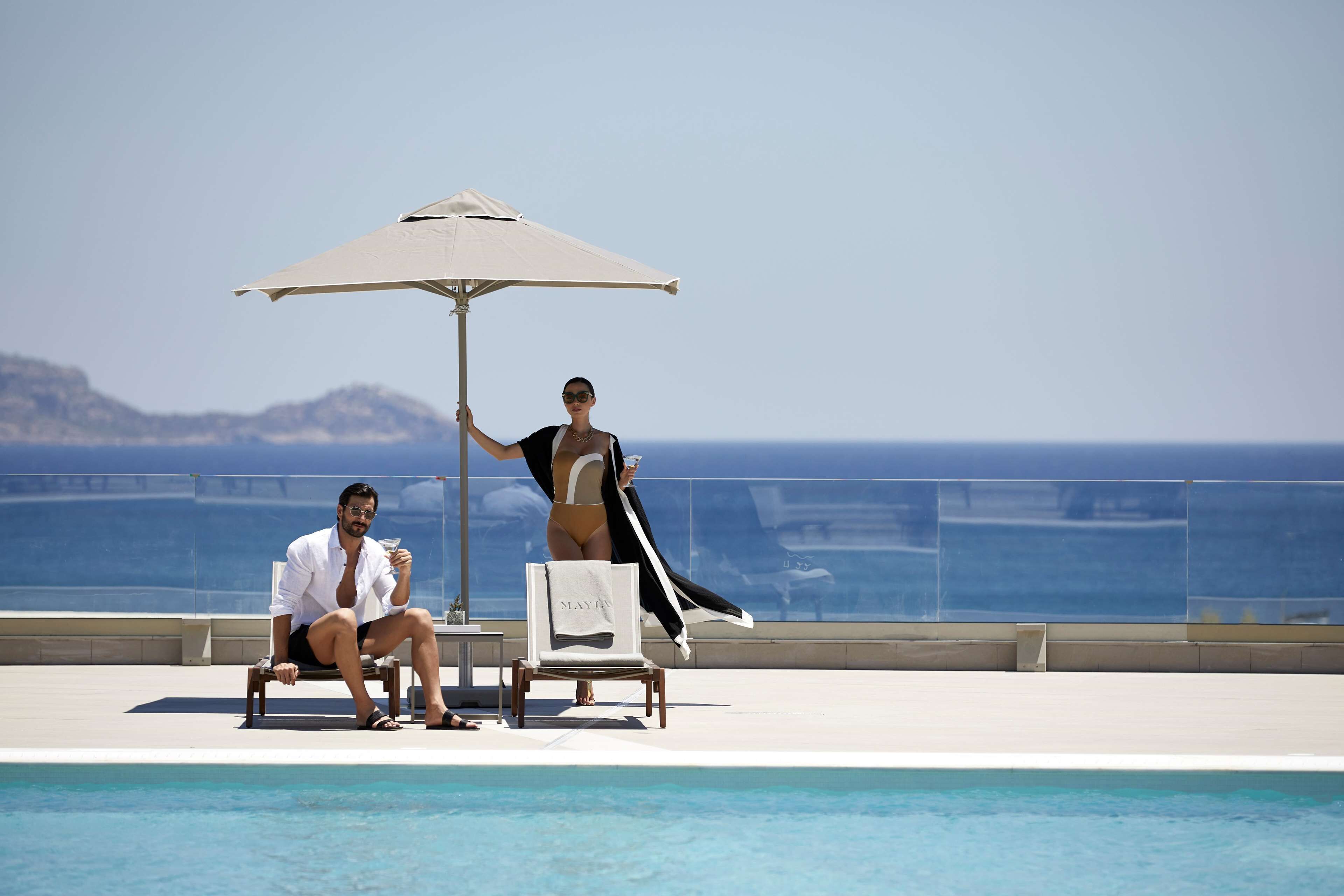 Two people sitting by a pool with a clear view of the sea and distant mountains.