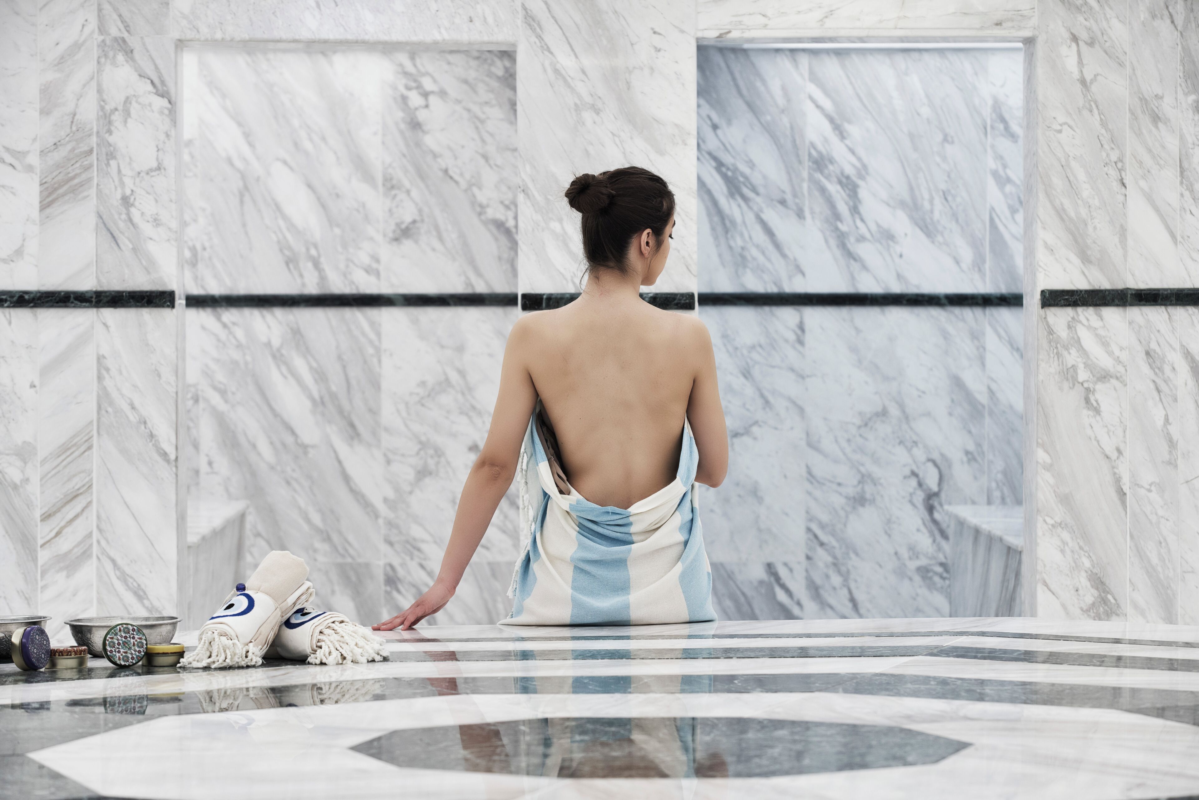 A person standing in a bathroom with marble walls and a tiled floor.