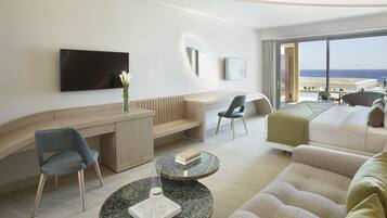 A modern hotel room with a curved desk, seating area, and a large window offering a view of the ocean.