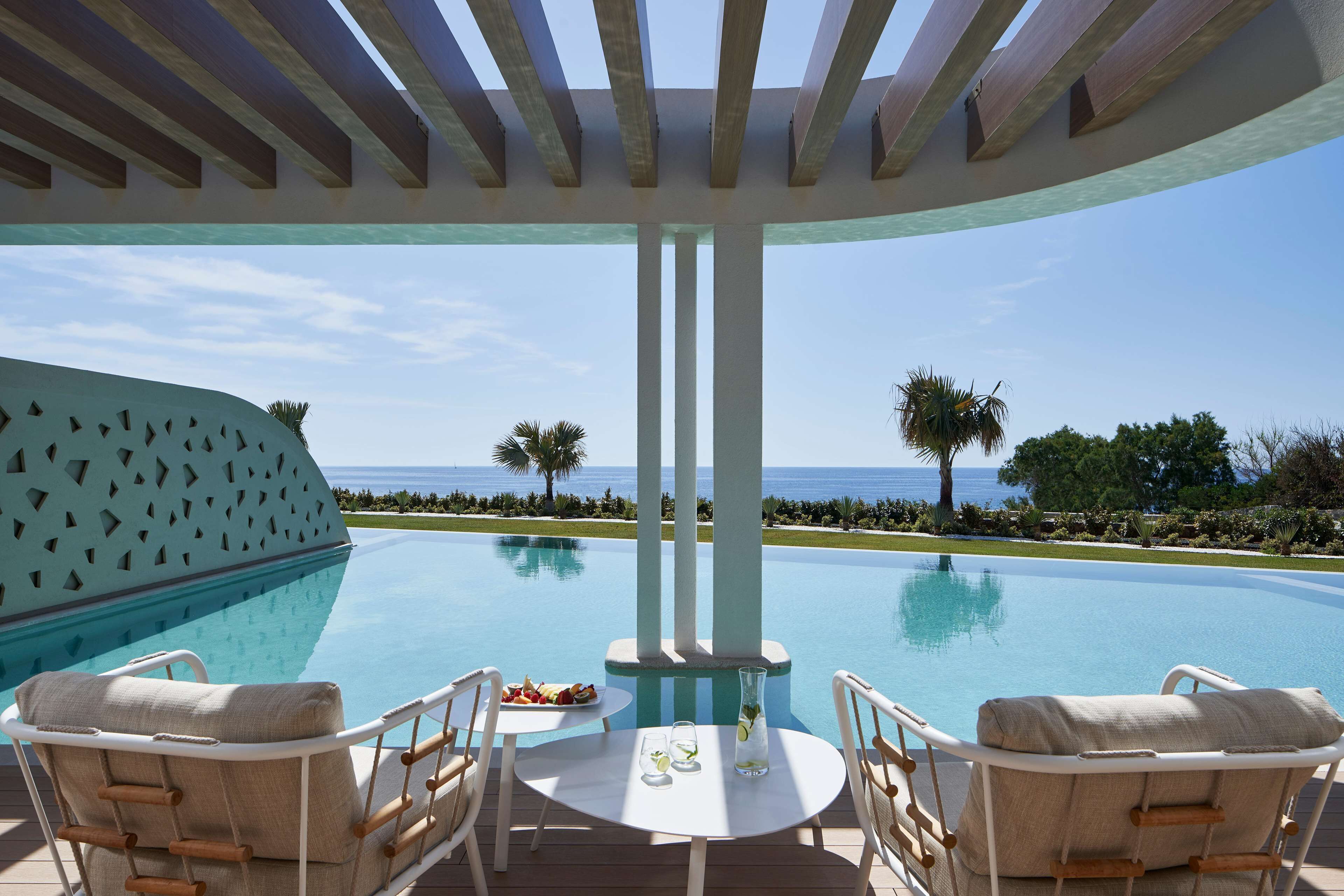 A poolside area with a view of the ocean, a table with a drink, and two lounge chairs.