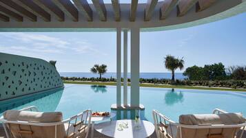 A poolside area with a view of the ocean, a table with a drink, and two lounge chairs.