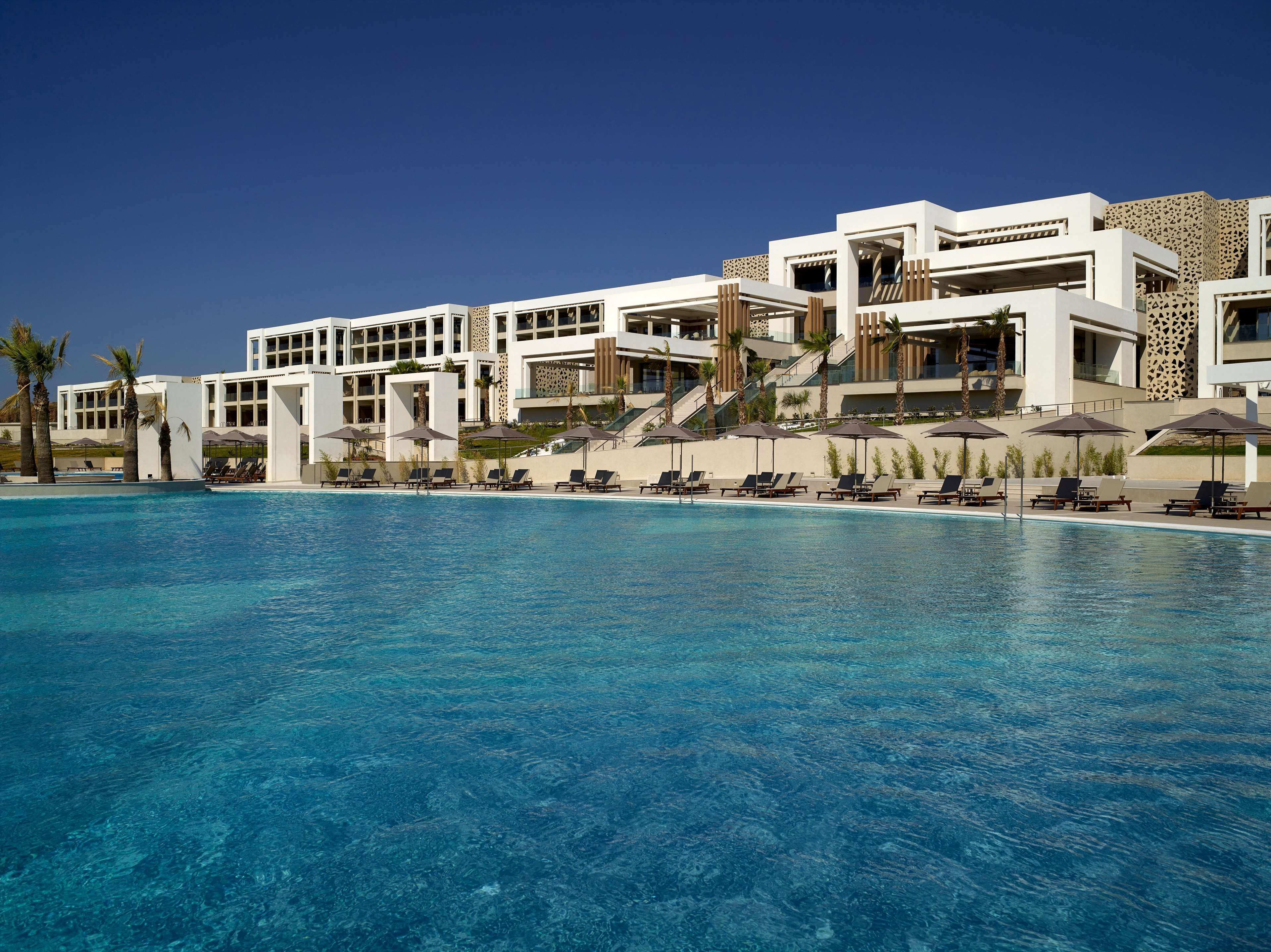 Un hotel moderno con una piscina grande, tumbonas y palmeras.