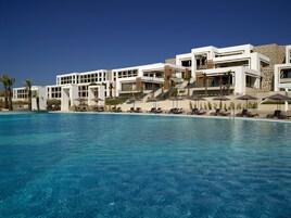 Un hotel moderno con una piscina grande, tumbonas y palmeras.