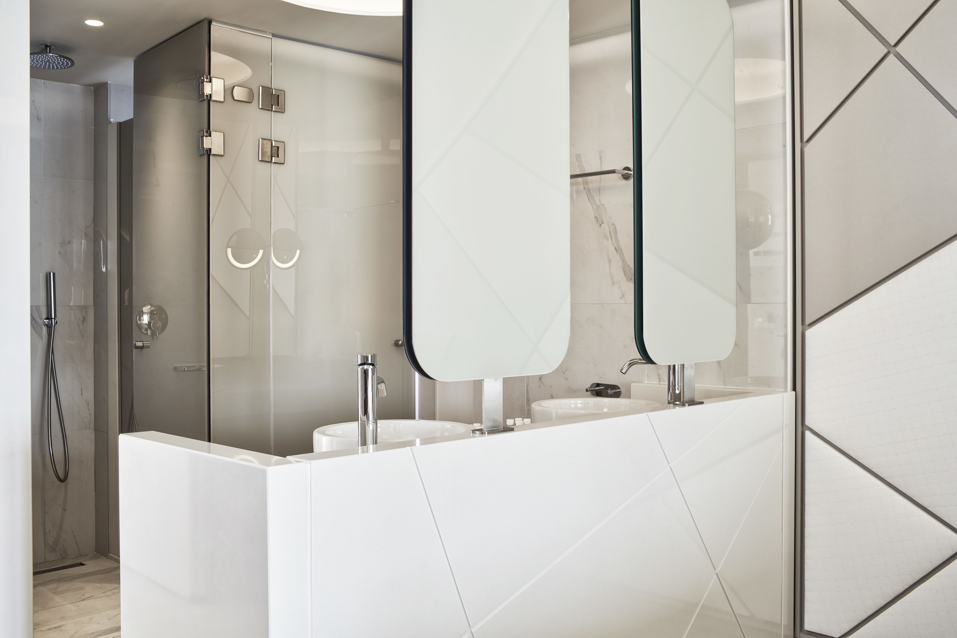 Un baño moderno con cabina de ducha de vidrio, tocador blanco con dos lavamanos y un espejo grande.