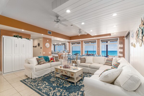 A spacious living room with white furniture, a large window overlooking the ocean, and a ceiling fan. - Xanadu:  ON.THE.BEACH! Heated pools, Ocean2River, Elevator, Dock,Spa: It's HUGE! (Stuart)