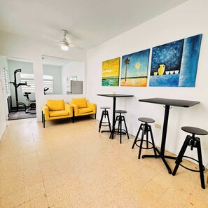 Un salon avec un canapé jaune, un ventilateur de plafond et un mur orné de trois tableaux.