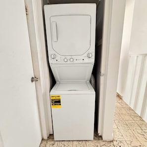 Une machine à laver blanche se trouve dans un couloir étroit, avec une porte sur un des côtés.