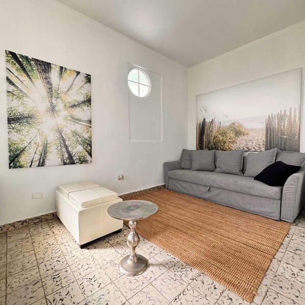A living room with a grey sofa, a white ottoman, a round table, and two large wall-mounted artworks.