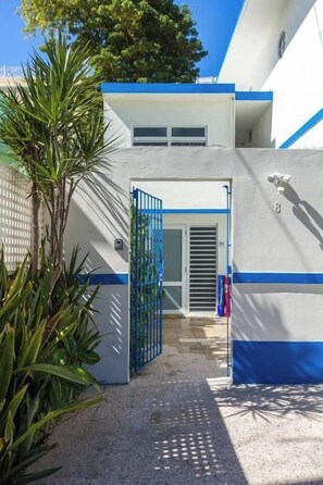 A gated entrance to a building with a blue and white color scheme, a clear sky, and a palm tree in the foreground.